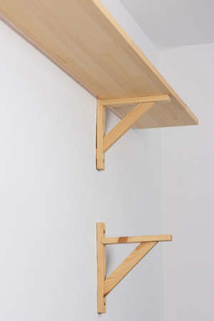The process of attaching a wooden shelf to the wall, shelf corners together with a bookshelfの写真素材