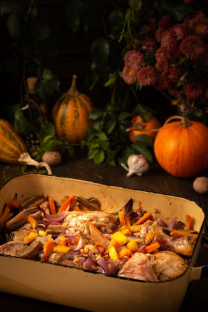 Baked chicken with vegetables in an iron brazier on a dark wooden background, chicken drumsticks with eggplant, pumpkin, onions and carrots baked in the ovenの写真素材
