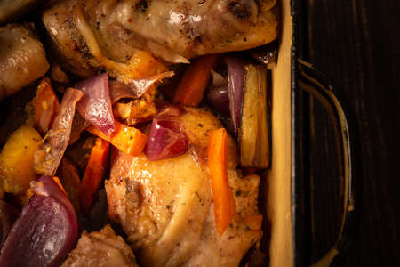 Baked chicken with vegetables in an iron brazier on a dark wooden background, chicken drumsticks with eggplant, pumpkin, onions and carrots baked in the ovenの写真素材