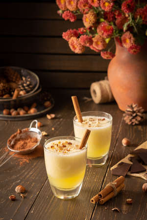 Refreshing delicious melon smoothie with cinnamon, hazelnuts and chocolate, vase of chrysanthemums and glasses of smoothie on wooden backgroundの写真素材