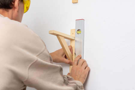 A man hangs a shelf in an apartment on a white wall, a worker checks the evenness of the shelf with a spint levelの写真素材