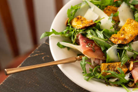 Light autumn salad with arugula, baked pumpkin, prosciutto and young parmesan, a plate of salad on a wooden tableの写真素材