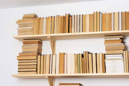 Light wooden bookshelves with hardback overturned books in white interior, home libraryの写真素材