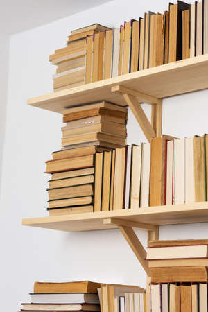 Light wooden bookshelves with hardback overturned books in white interior, home libraryの写真素材