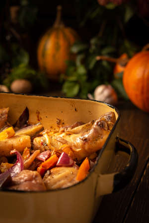 Baked chicken with vegetables in an iron brazier on a dark wooden background, chicken drumsticks with eggplant, pumpkin, onions and carrots baked in the ovenの写真素材