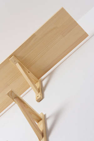 The process of attaching a wooden shelf to the wall, shelf corners together with a bookshelfの写真素材