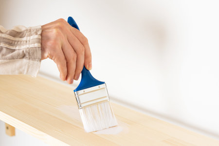Painter varnishes the bookshelf, male hand with paint brush