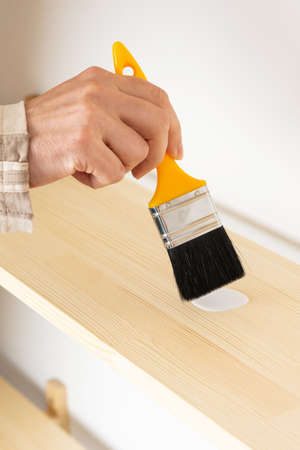 Painter varnishes the bookshelf, male hand with paint brushの写真素材