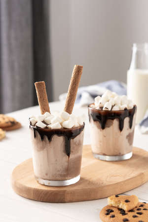 Milkshake with ice cream, marshmallows and chocolate, a glass with a milkshake on a wooden board, chocolate chip cookies and a bottle of milkの写真素材