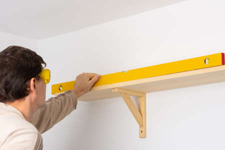 A man hangs a shelf in an apartment on a white wall, a worker checks the evenness of the shelf with a spint levelの写真素材