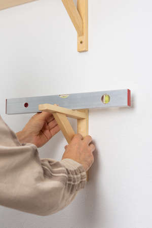 A man hangs a shelf in an apartment on a white wall, a worker checks the evenness of the shelf with a spint levelの写真素材