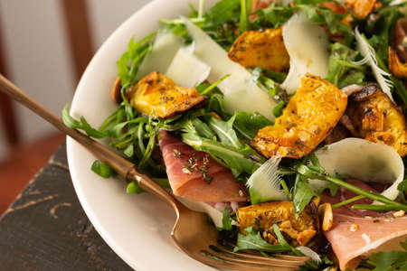 Light autumn salad with arugula, baked pumpkin, prosciutto and young parmesan, a plate of salad on a wooden tableの写真素材