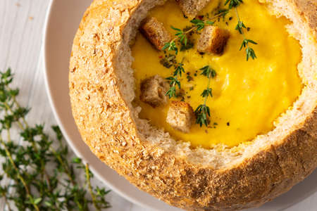 Pumpkin puree soup in a plate of bread close up, pumpkin soup with thyme , cheese and croutons on a white wooden background, top viewの写真素材