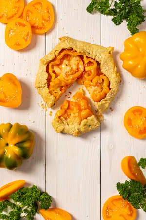 Pie with yellow tomatoes , bell peppers and sesame seeds, galette with vegetables and cheese on white wooden background, top viewの写真素材