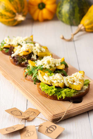 Toasted sandwiches with brie cheese, baked pumpkin and salad, arugula and mozzarella, delicious vegetable snacks on a wooden boardの写真素材