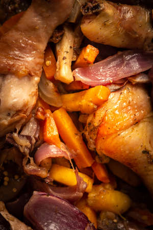 Baked chicken with vegetables in an iron brazier on a dark wooden background, chicken drumsticks with eggplant, pumpkin, onions and carrots baked in the ovenの写真素材