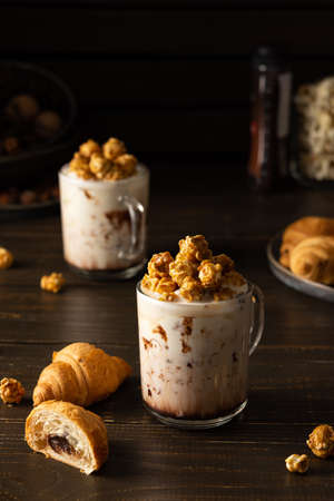 Glass mugs with chocolate milkshake and caramel popcorn and chocolate croissants on wooden backgroundの写真素材