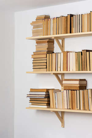 Light wooden bookshelves with hardback overturned books in white interior, home libraryの写真素材