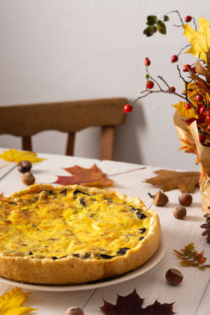Quiche pie with mushrooms and cheese, autumn background with fallen maple and oak leaves, pine cones, rose hips and hazelnutsの写真素材
