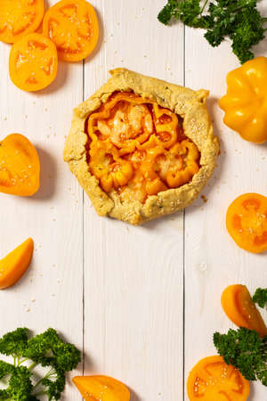 Pie with yellow tomatoes , bell peppers and sesame seeds, galette with vegetables and cheese on white wooden background, top viewの写真素材