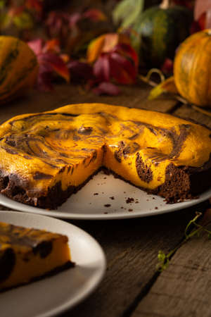 Chocolate pumpkin sweet pie on a wooden background, cake on a background of red leaves of grapes, pumpkins and autumn bouquet in a vaseの写真素材