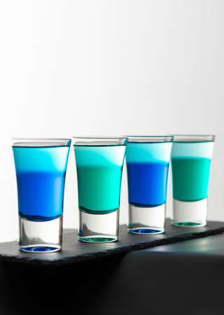 Blue and green alcoholic shots, shot glasses with colored liquor on a black board close upの写真素材