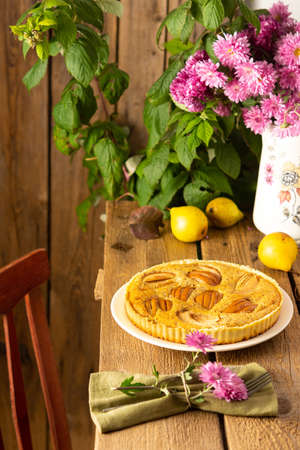 Delicious pear pie from yellow pears on a wooden background, raspberry bush in the background, pink chrysanthemums in a vase, rustic styleの写真素材