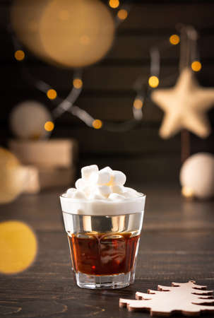 Festive alcoholic shot with marshmallows, concept of christmas or new year, decoration of christmas balls, glowing garland and gifts in neutral natural colorsの写真素材