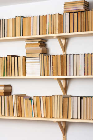 Light wooden bookshelves with hardback overturned books in white interior, home libraryの写真素材