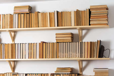 Light wooden bookshelves with hardback overturned books in white interior, home libraryの写真素材