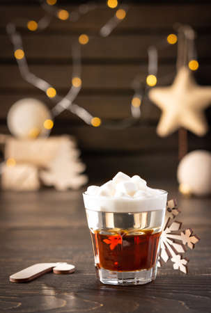 Festive alcoholic shot with marshmallows, concept of christmas or new year, decoration of christmas balls, glowing garland and gifts in neutral natural colorsの写真素材