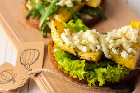 Toasted sandwiches with brie cheese, baked pumpkin and salad, arugula and mozzarella, delicious vegetable snacks on a wooden boardの写真素材