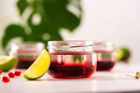 Red alcoholic shots on white background , small jars with liquor and grenadine with limeの写真素材