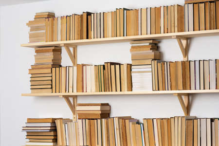 Light wooden bookshelves with hardback overturned books in white interior, home libraryの写真素材
