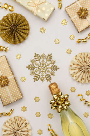Festive background with gold decoration , gift boxes with bottle of sparkling wine, shiny golden serpentine confetti and paper christmas tree decorations, glittering snowflakesの写真素材
