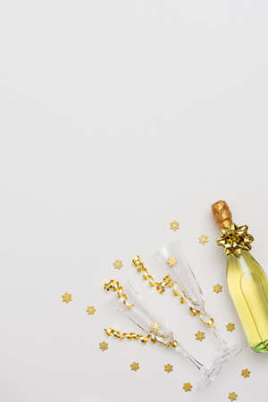 Festive white background with gold decoration , bottle of sparkling wine with two crystal glasses, shiny golden serpentine confetti and glittering snowflakes, copy space, top viewの写真素材