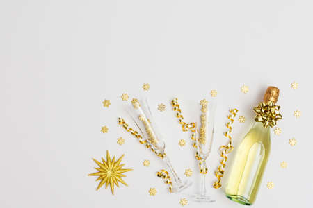 Festive white background with gold decoration , bottle of sparkling wine with two crystal glasses, shiny golden serpentine confetti and glittering snowflakes, golden star, copy space, top viewの写真素材