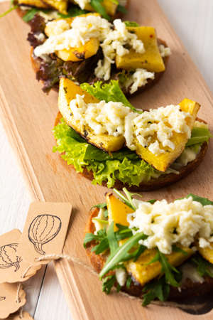 Toasted sandwiches with brie cheese, baked pumpkin and salad, arugula and mozzarella, delicious vegetable snacks on a wooden boardの写真素材