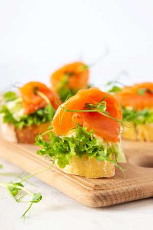 Canapes with mozzarella cheese, salad, salmon and pea sprouts, toast with red fish on a wooden board close upの写真素材