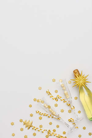 Festive white background with gold decoration , bottle of sparkling wine with two crystal glasses, shiny golden serpentine confetti and glittering snowflakes, copy space, top viewの写真素材