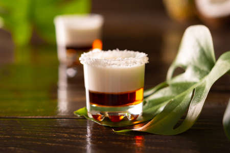 Tropical alcoholic shots decorated with coconut flakes, monstera flower with coconut and pineapple on brown wooden backgroundの写真素材