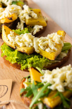 Toasted sandwiches with brie cheese, baked pumpkin and salad, arugula and mozzarella, delicious vegetable snacks on a wooden boardの写真素材