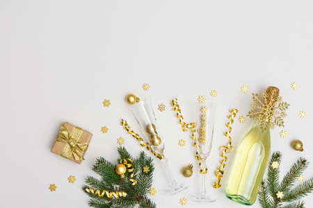 Festive background with gold decoration , bottle of sparkling wine with two crystal glasses, green spruce branches and shiny golden serpentine confetti ,glittering snowflakes and gift box, copy spaceの写真素材