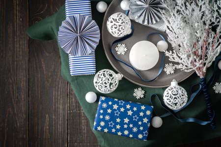 Christmas composition in white ,green and blue shades, christmas balls and candle, gift boxes and snowflakes, decorative white spruce branches and snowball on a green tablecloth, top view, copy spaceの写真素材
