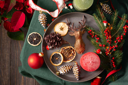 Christmas or new year background, christmas tree decorations and candle, dried fruits and decorative deer, spruce and cotoneaster branches on a green tablecloth, poinsettia flower , top viewの写真素材