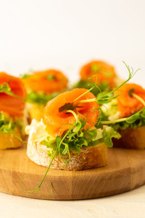 Canapes with mozzarella cheese, salad, salmon and pea sprouts, toast with red fish on a wooden board close upの写真素材
