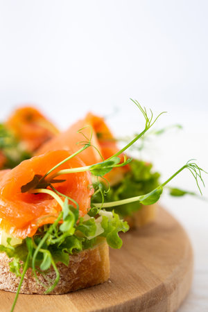 Canapes with mozzarella cheese, salad, salmon and pea sprouts, toast with red fish on a wooden board close upの写真素材