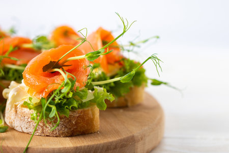 Canapes with mozzarella cheese, salad, salmon and pea sprouts, toast with red fish on a wooden board close upの写真素材