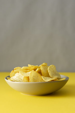Crispy chips on a gray plate on a yellow table against a gray wall background, trendy colors of the yearの写真素材
