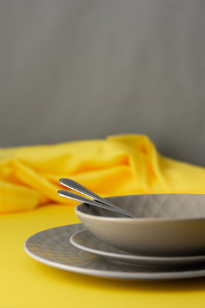 Table setting in trendy colors of the year, gray plates and a fork with a spoon on a yellow background with a yellow tableclothの写真素材